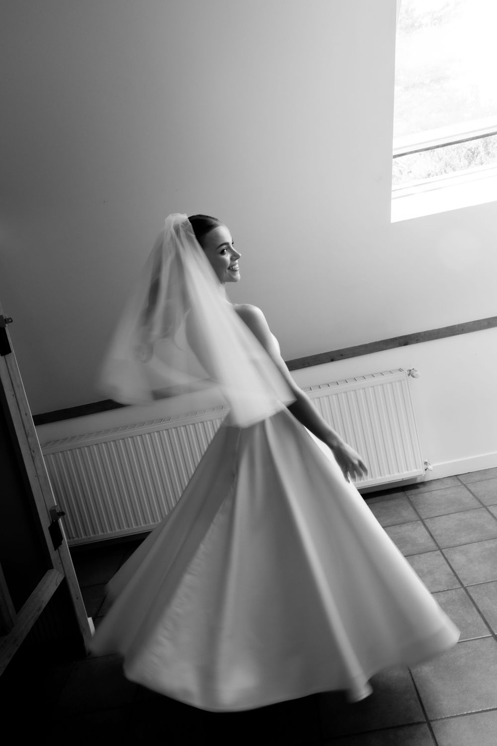 Bride in white gown and veil twirling in black and white wedding photo indoors.