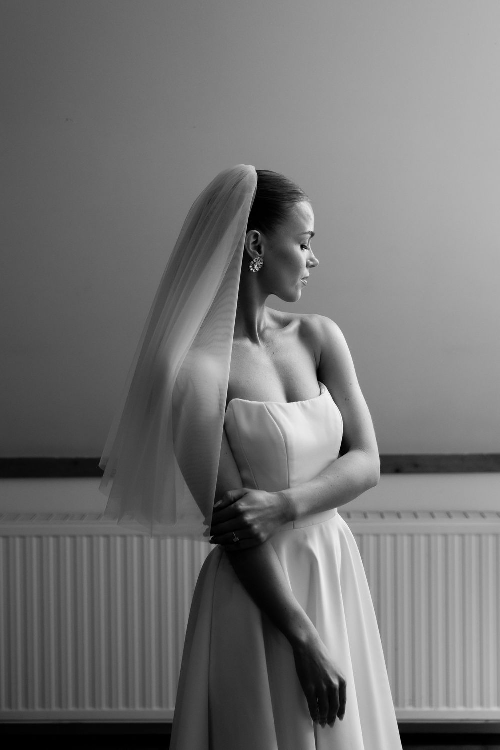 Elegant bride in strapless gown and veil poses in black and white portrait.