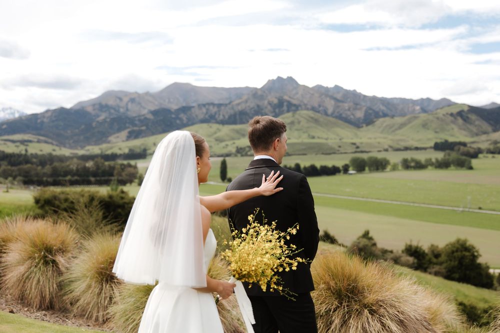 Bride and groom overlooking lush green mountains and valleys on their wedding day in New Zealand.