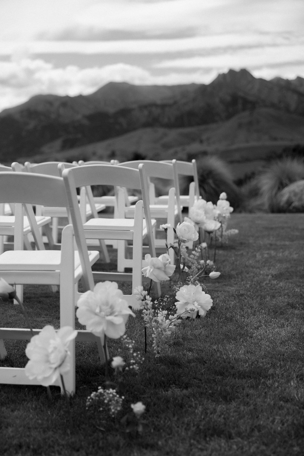 Elegant outdoor wedding ceremony setup with white chairs and floral arrangements against mountain backdrop.