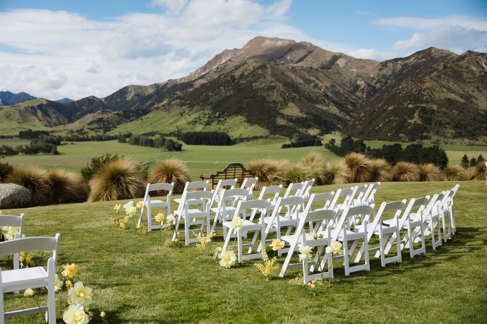 Outdoor wedding ceremony setup with white chairs on green lawn against stunning mountain scenery.