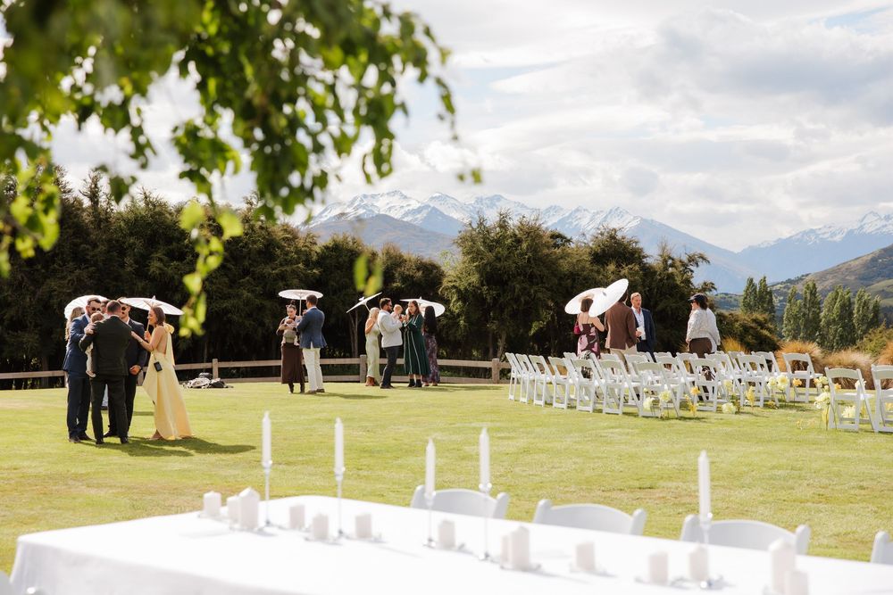 Outdoor wedding ceremony on green lawn with mountain views, white chairs and candle centerpieces.