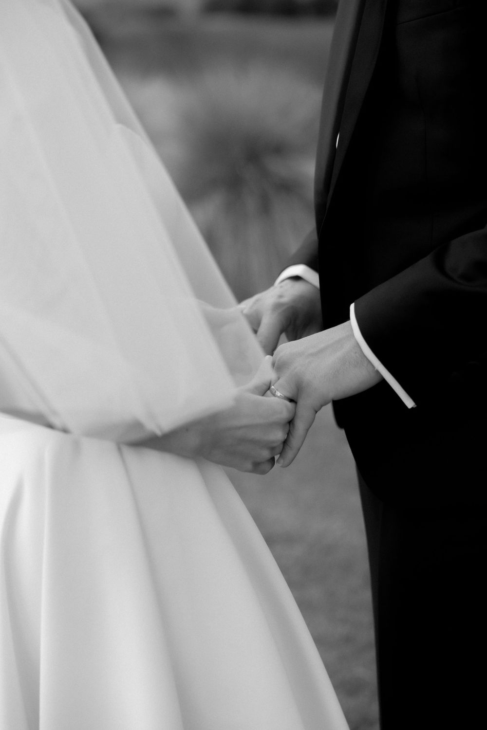 Close-up black and white photo of bride and groom holding hands during wedding ceremony.