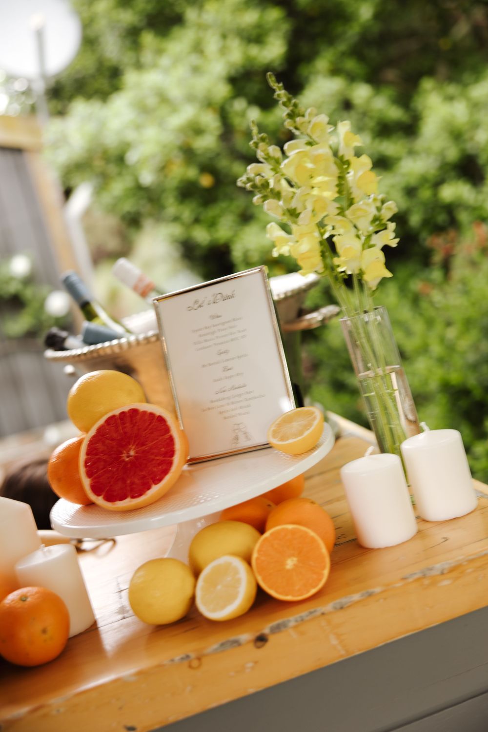 Elegant wedding cocktail table decorated with fresh citrus fruits, yellow flowers, and a framed menu.