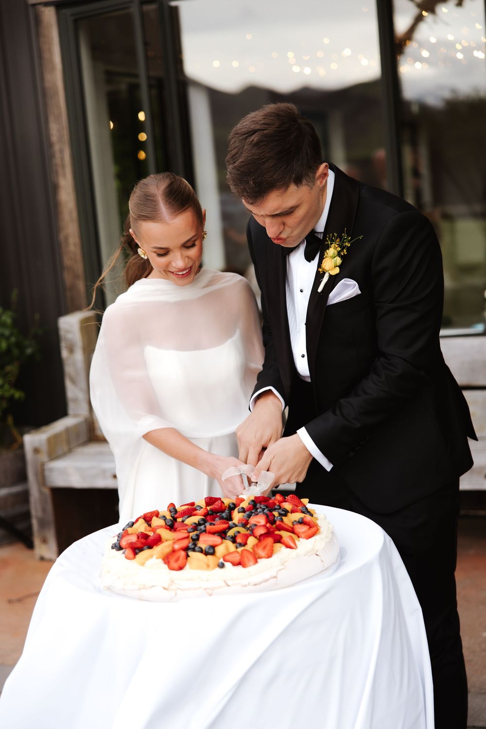 Bride and groom cutting their wedding pavlova cake topped with fresh strawberries and blueberries.