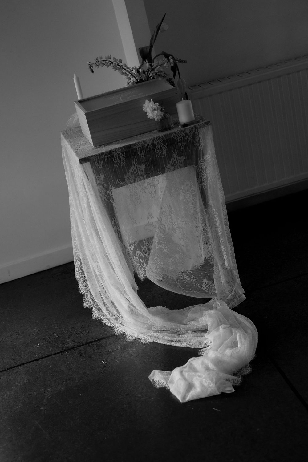Black and white photo of lace wedding veil draped over ceremony altar with candle and flowers.