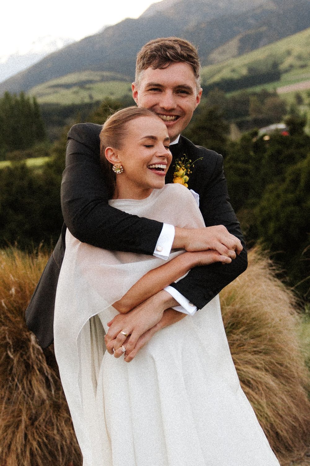 Happy couple embracing outdoors on their wedding day with stunning mountain scenery behind them.