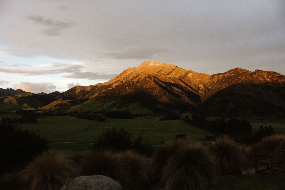 Golden sunset light illuminating dramatic mountain peaks above lush green valley in New Zealand.