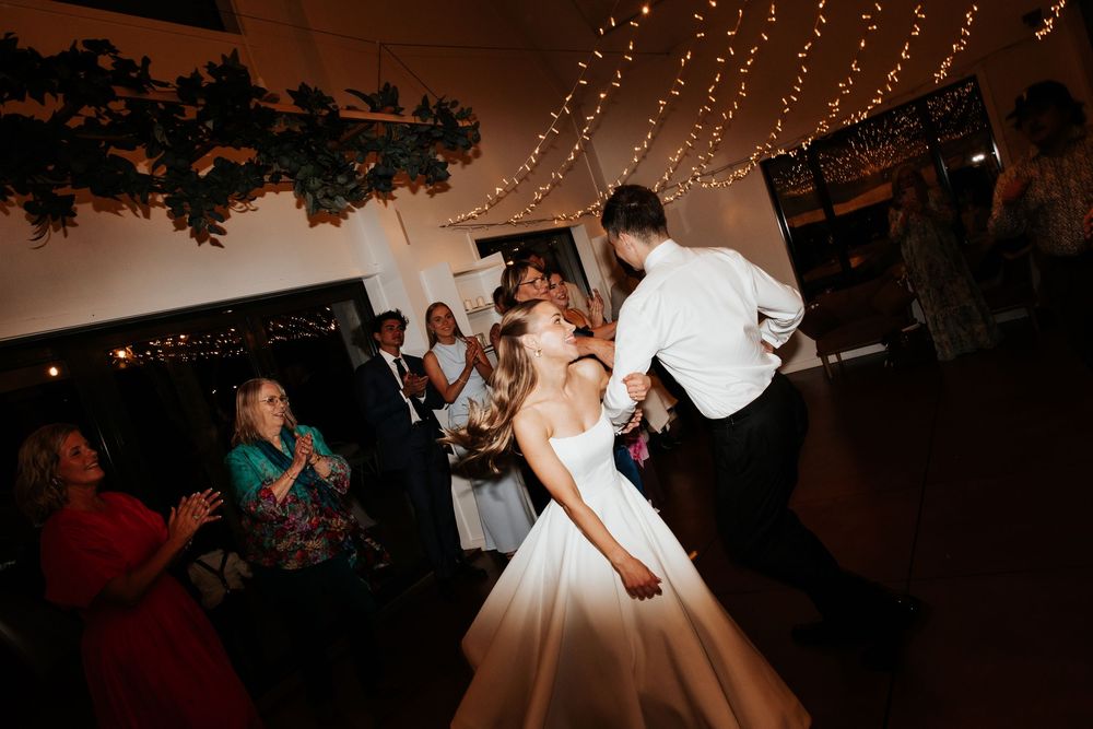 Bride and groom sharing a romantic first dance under warm fairy lights surrounded by wedding guests.