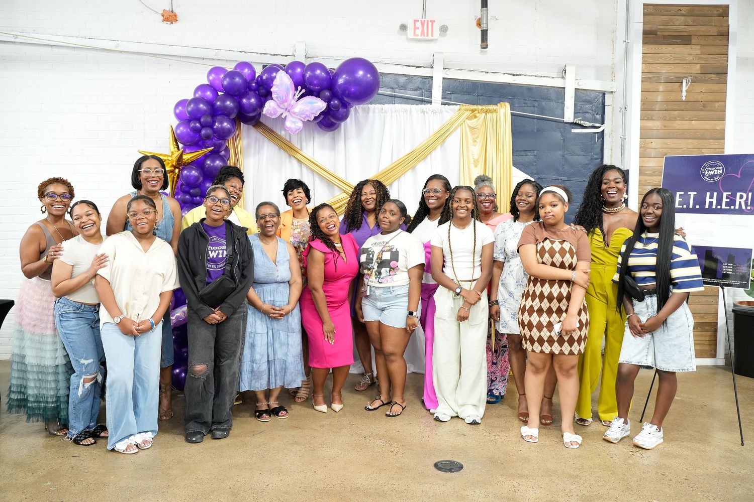 Group of women posing together at E.T.H.E.R. event with purple and gold balloon arch decoration.