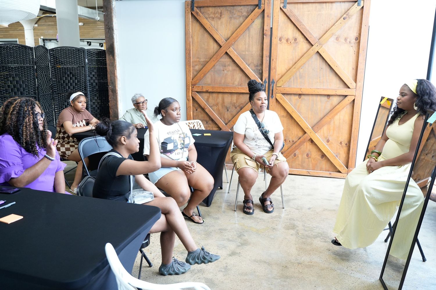 Women engaged in discussion at an indoor community workshop event with rustic barn door backdrop.