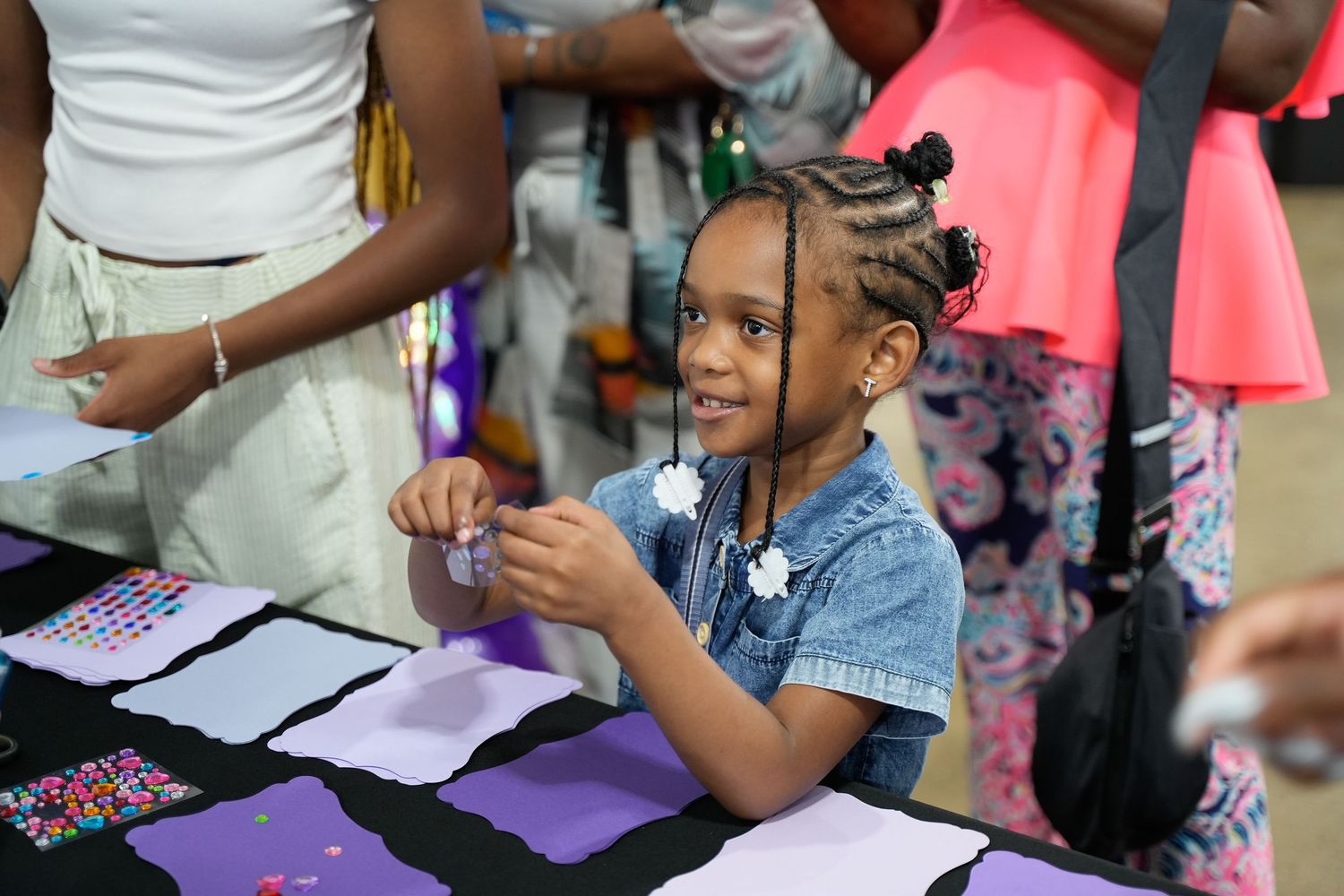 Young girl smiles while crafting at a colorful activity table during a community event.
