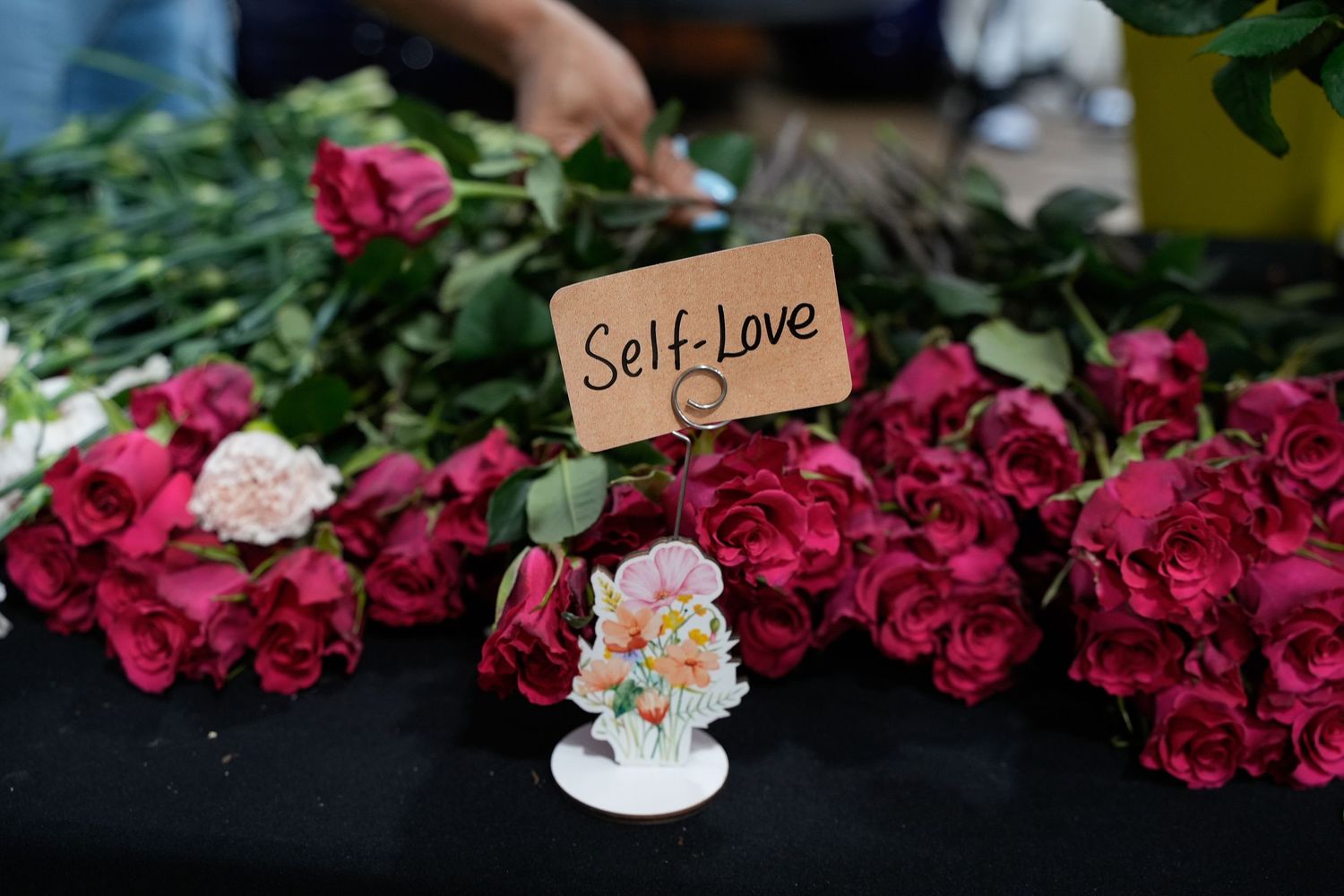 Vibrant red roses displayed on a table with a Self-Love sign at a floral event.