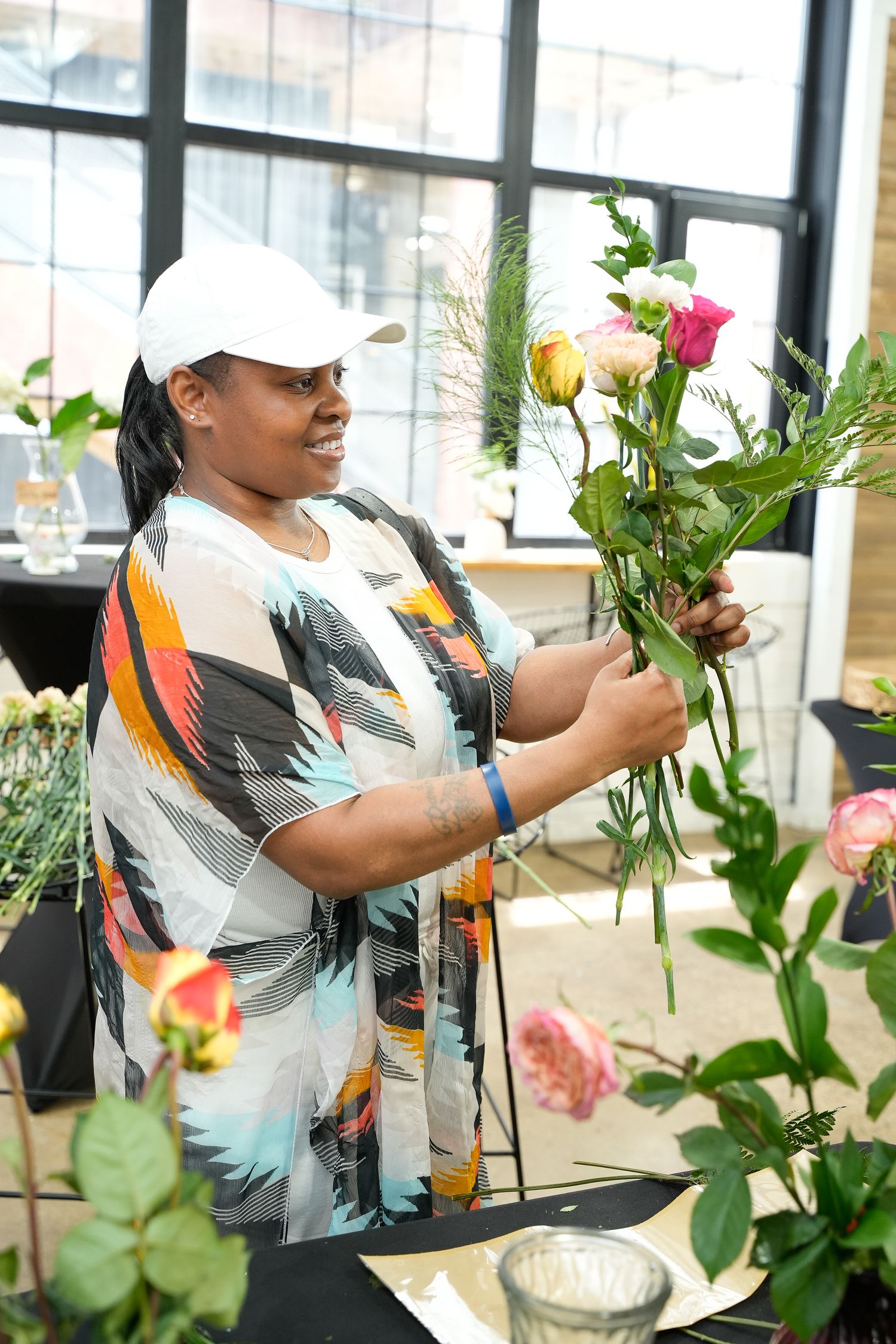 Woman in colorful top arranges fresh roses and flowers at a floral design workshop.