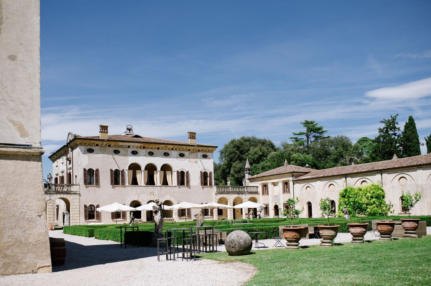 Elegant Italian villa with manicured gardens, terracotta pots, and outdoor dining area under blue skies.