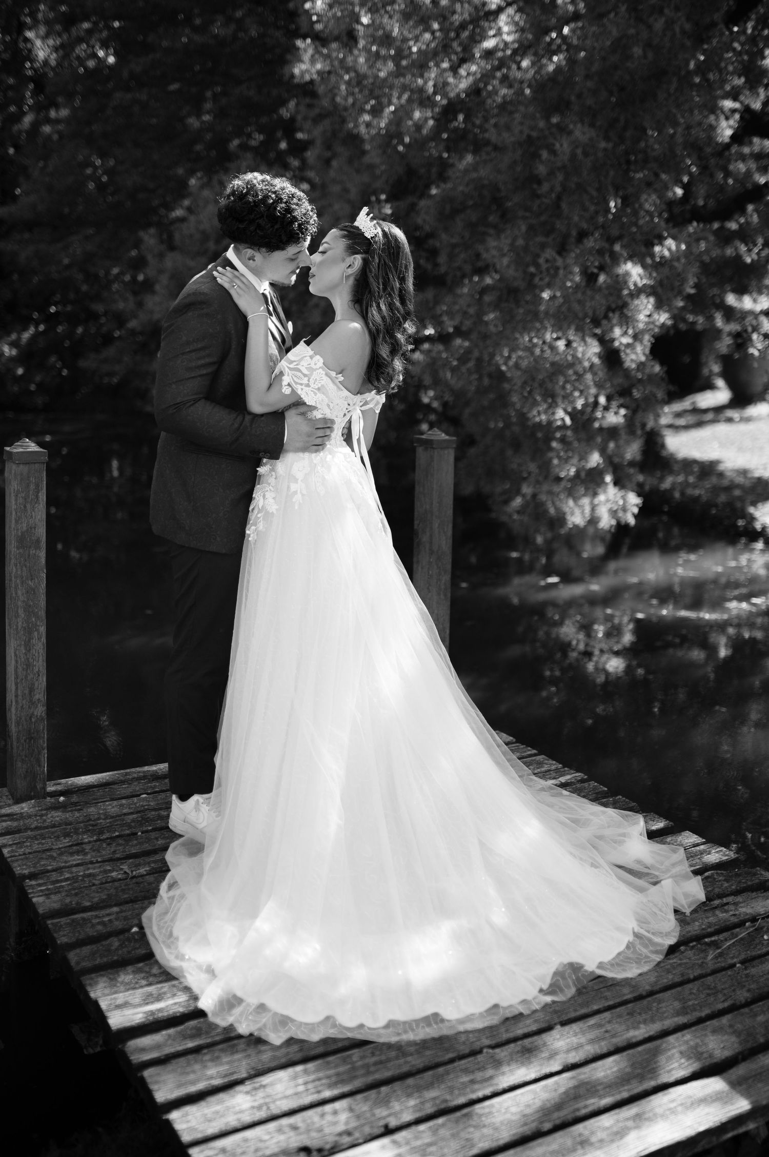 Black and white photo of bride and groom kissing on wooden dock, her flowing tulle gown trailing behind.