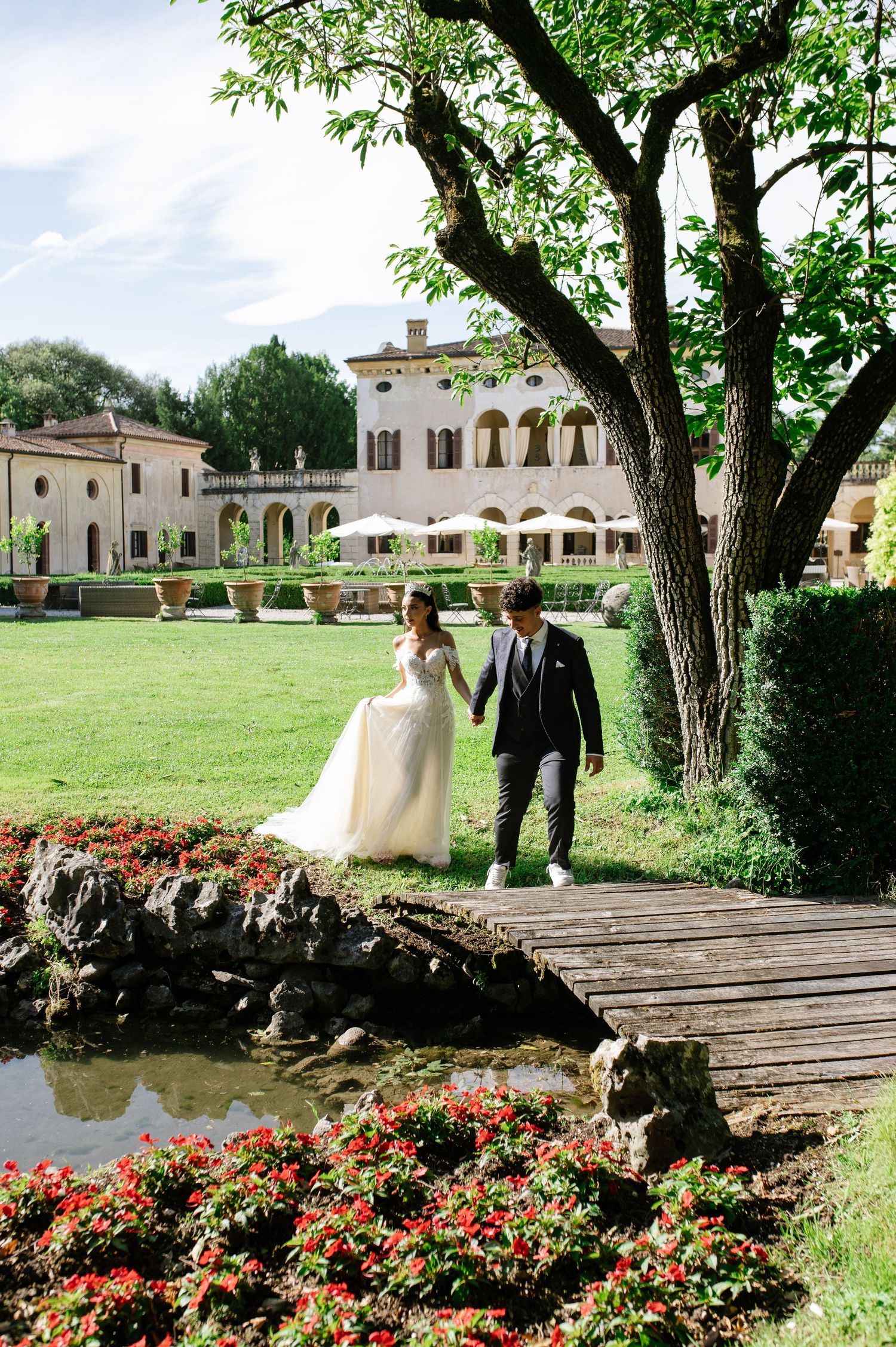 Bride and groom walk hand in hand through lush garden grounds of elegant Italian villa wedding venue.