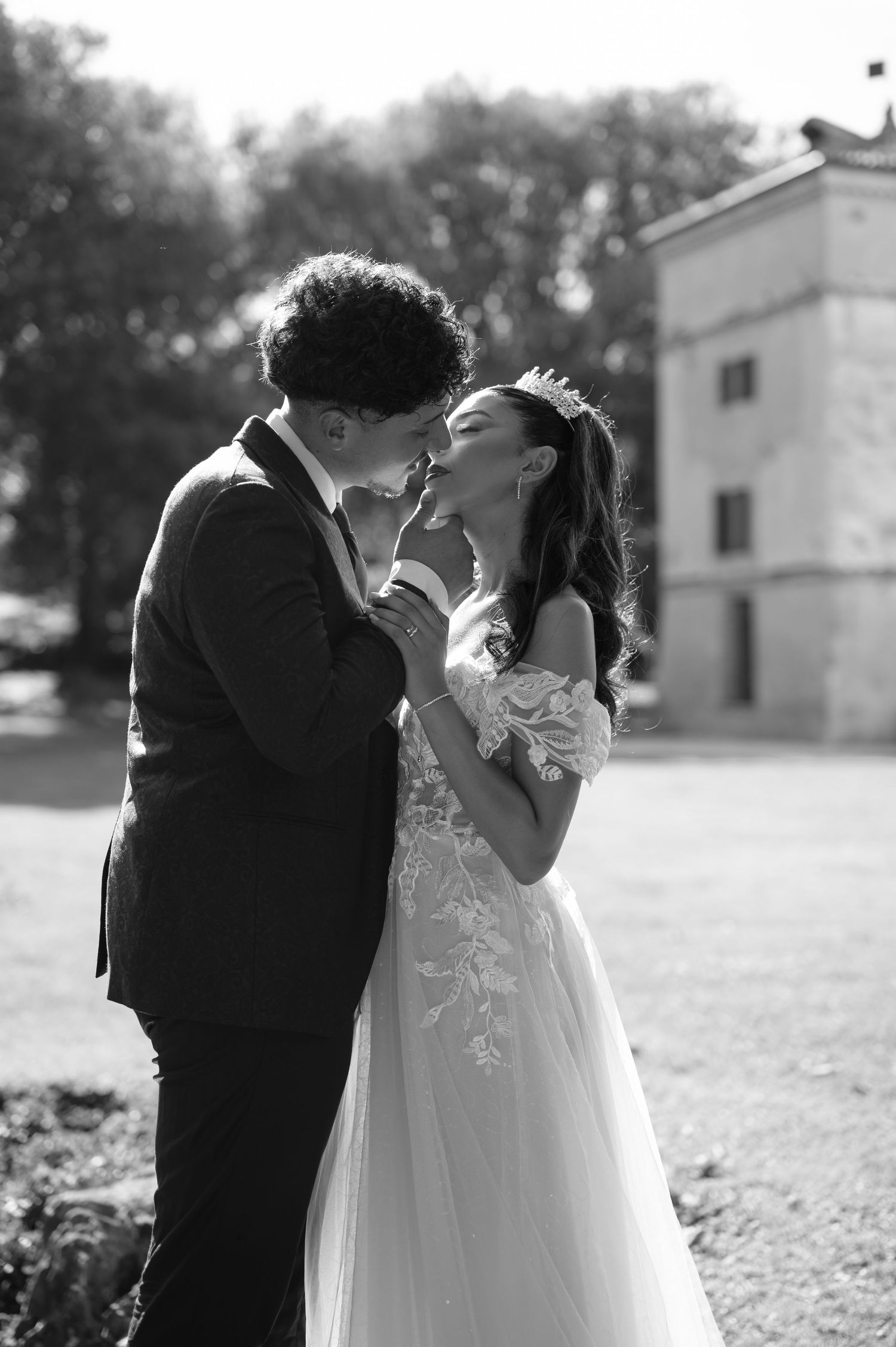 Black and white photo of bride and groom sharing a romantic kiss outdoors near a historic building.