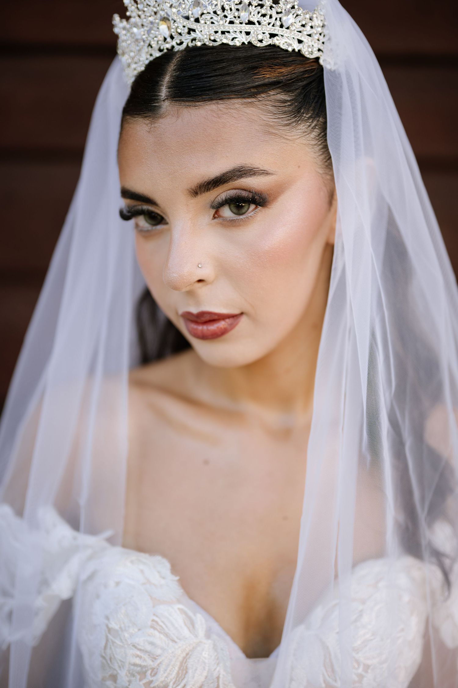 Beautiful bride wearing ornate crystal tiara and white veil with dramatic eye makeup and red lips.