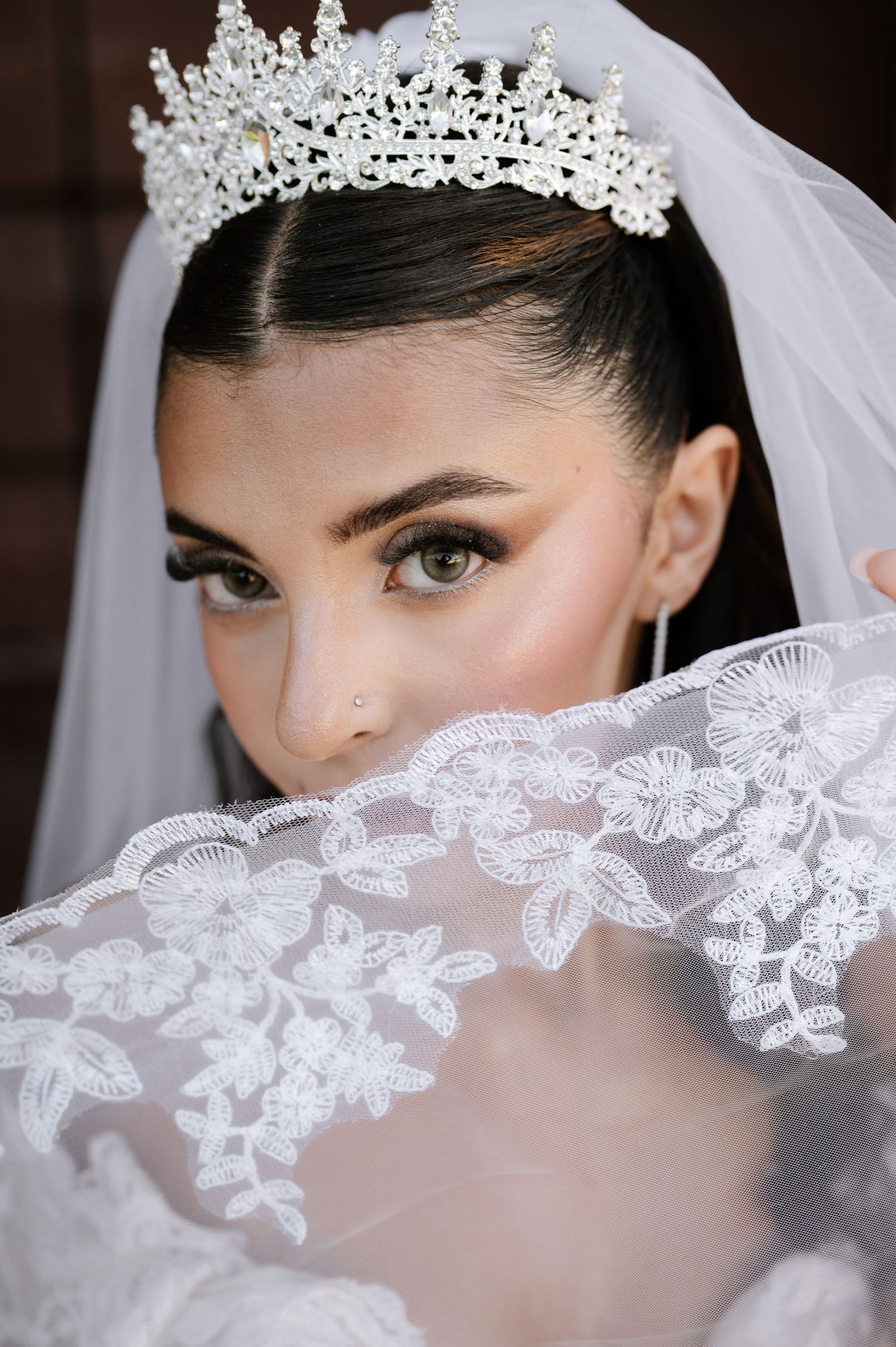 Bride wearing a crystal tiara and lace veil, showcasing elegant bridal makeup and dark hair.