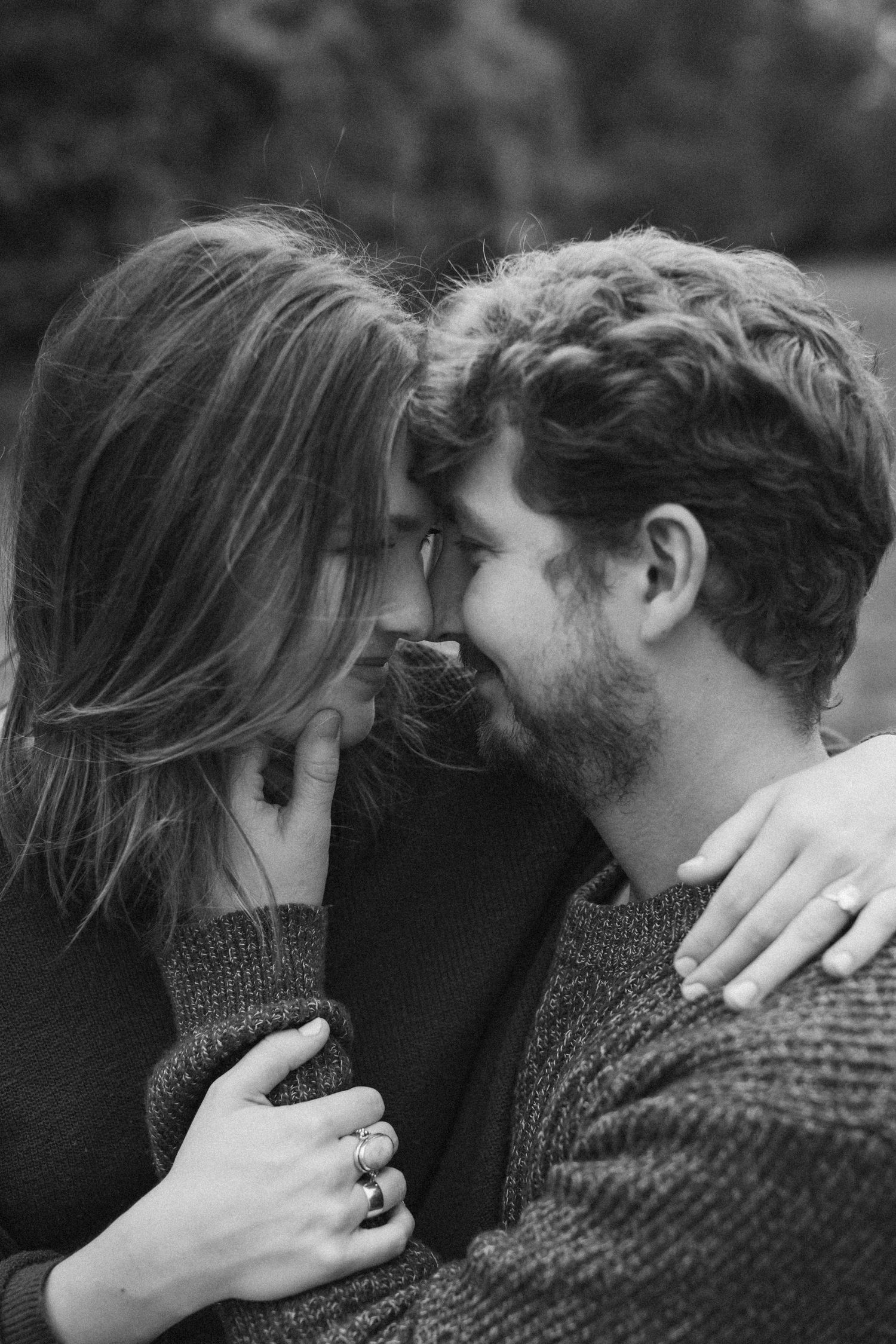 A man and woman gently touch their foreheads together and softly smile in an intimate, black-and-white engagement photo.