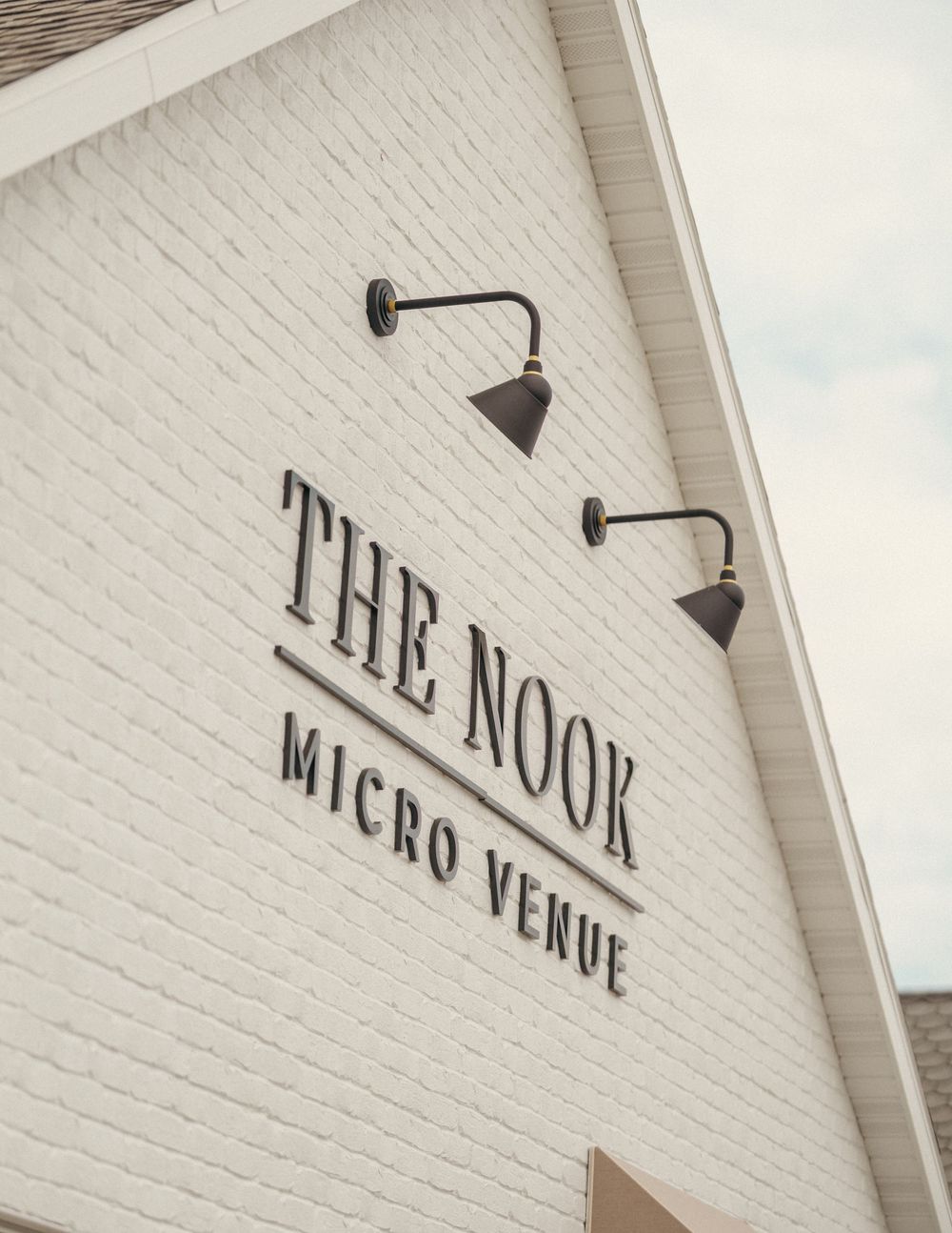 The Nook Micro Venue sign on a white brick wall with black gooseneck lights.