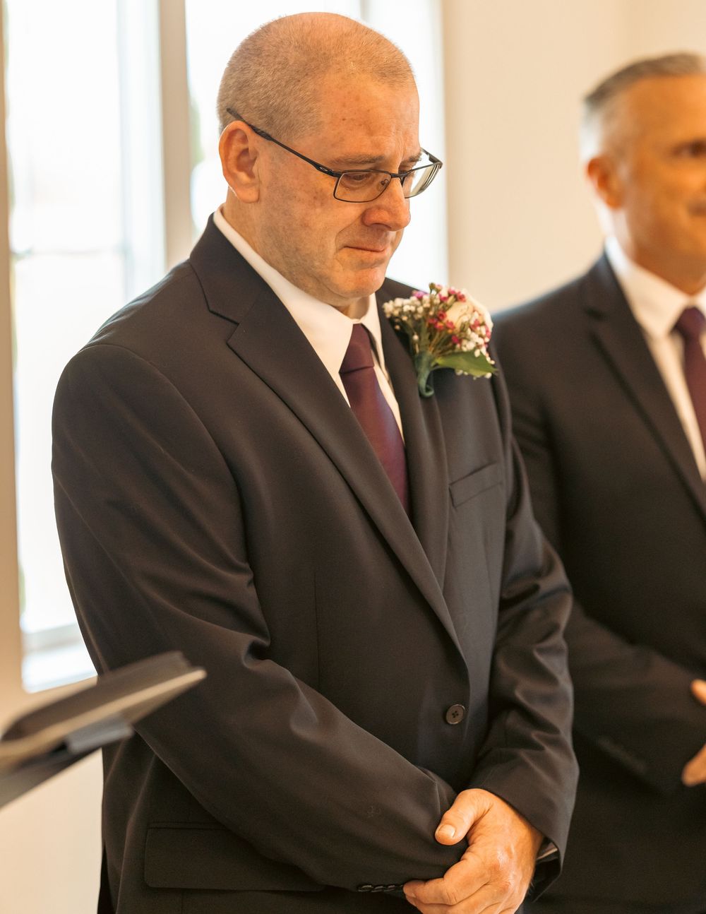 Emotional groom in dark suit with boutonniere standing at wedding altar.