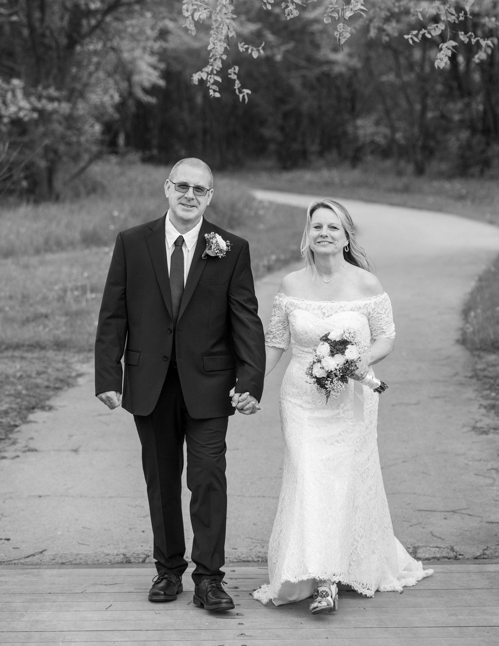 Bride and groom walk hand in hand on a park path in this classic black and white wedding portrait.