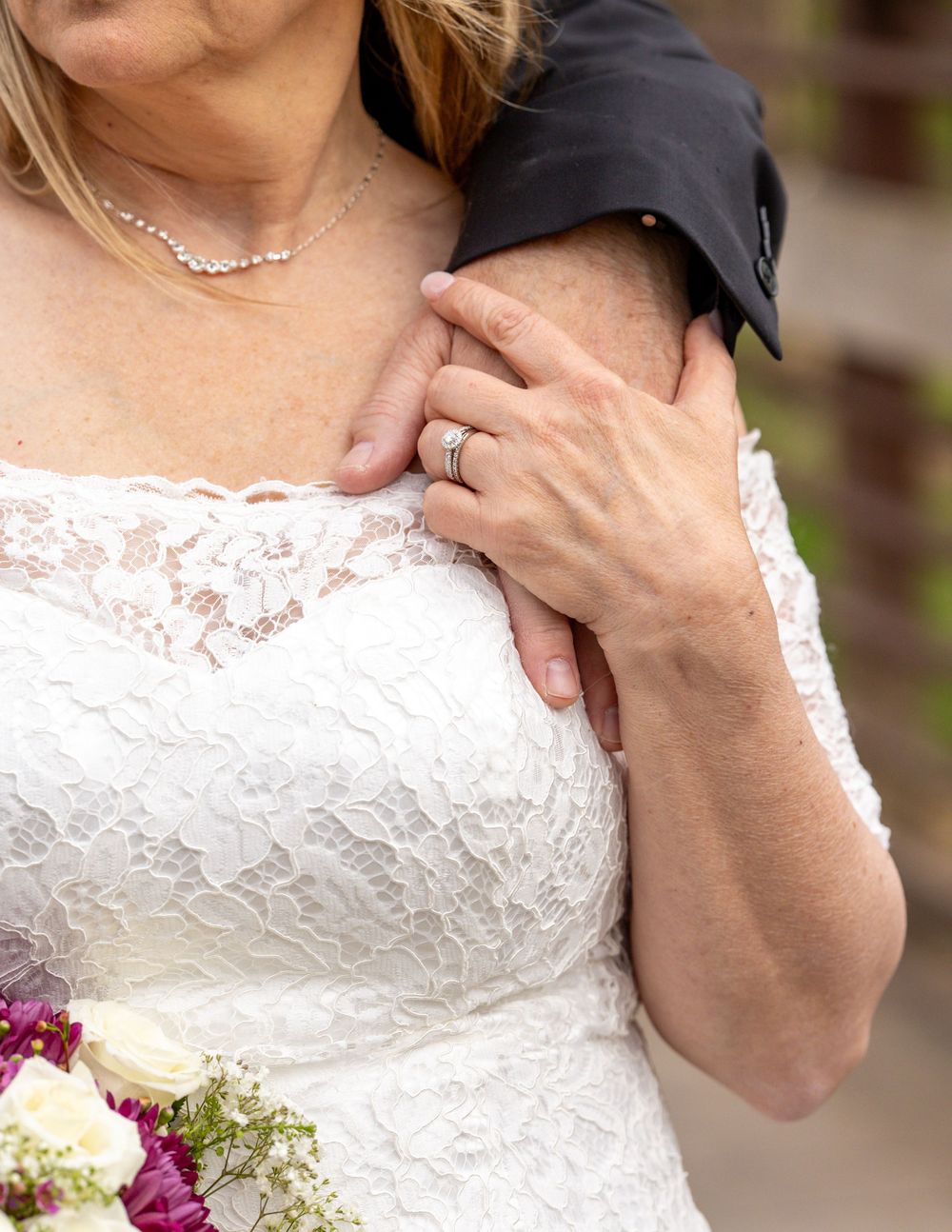Close-up of bride in lace dress with pearl necklace and wedding ring holding bouquet.