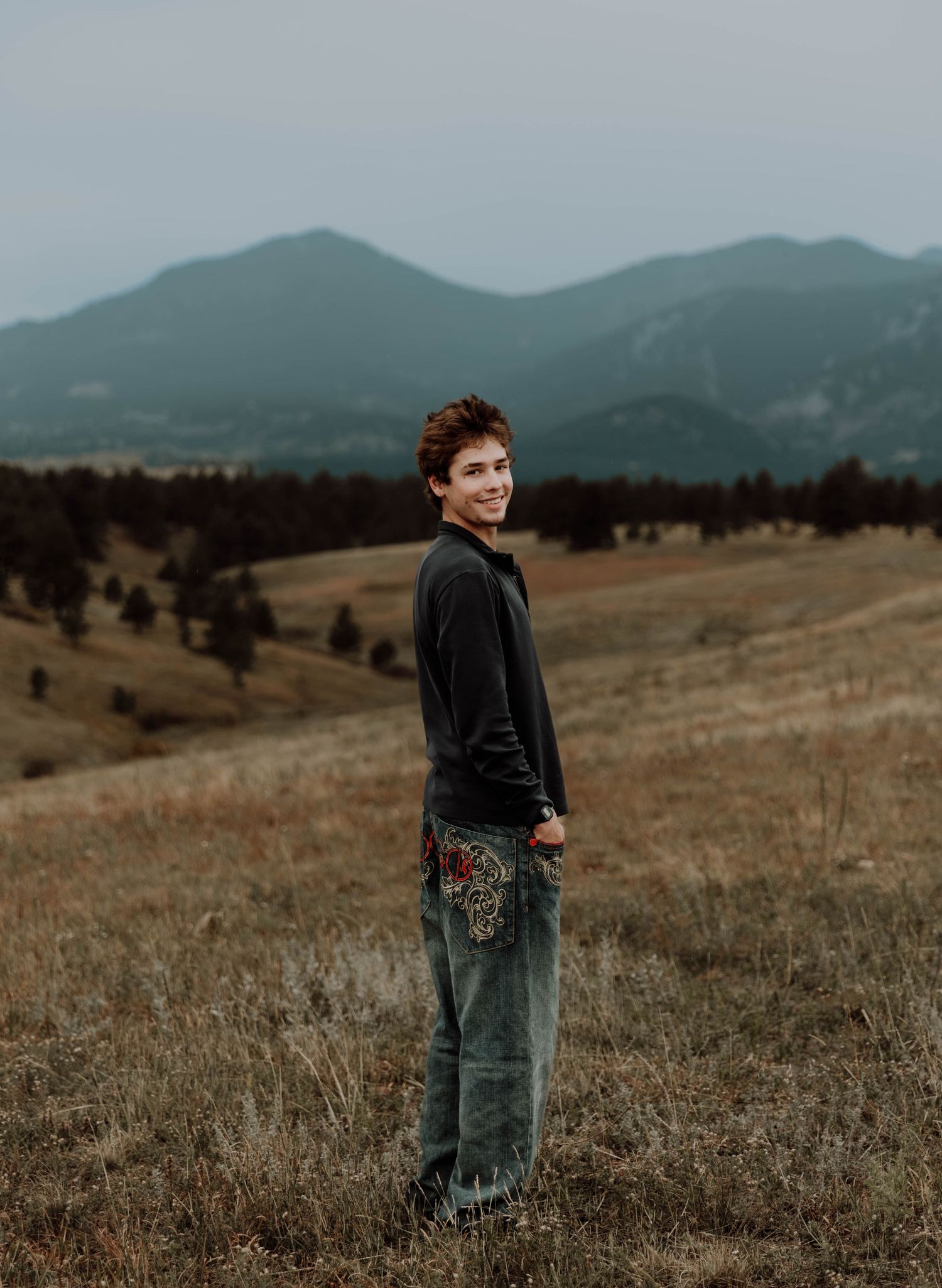 Boy stands, smiles, and poses for senior photos, cinematic, mountain, and portrait photos in Boulder, Colorado outside and in nature