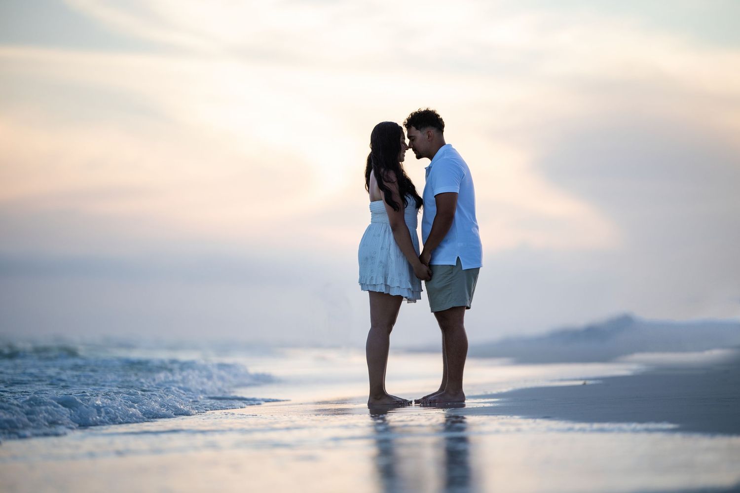 couple being photographed hugging during sunset at the water and beach line