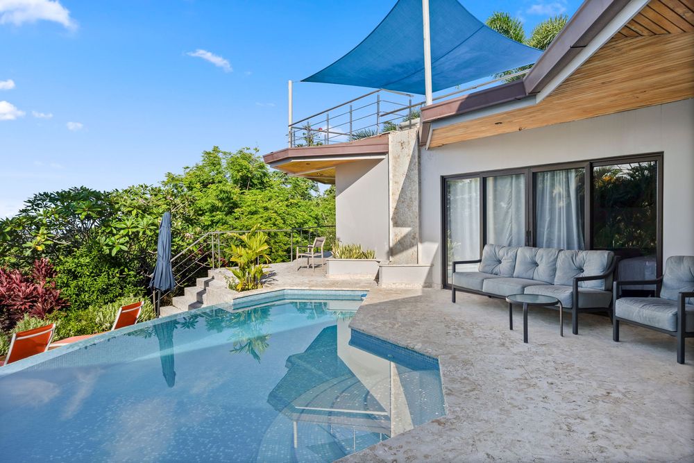 Luxury villa with infinity pool, outdoor seating area, and blue shade sail surrounded by tropical greenery VRBO and AirBnB