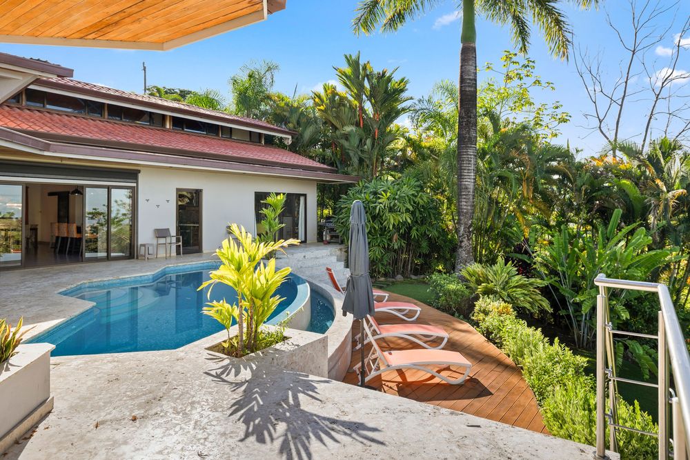 Tropical villa with a blue swimming pool surrounded by lush palm trees and a wooden deck patio area.