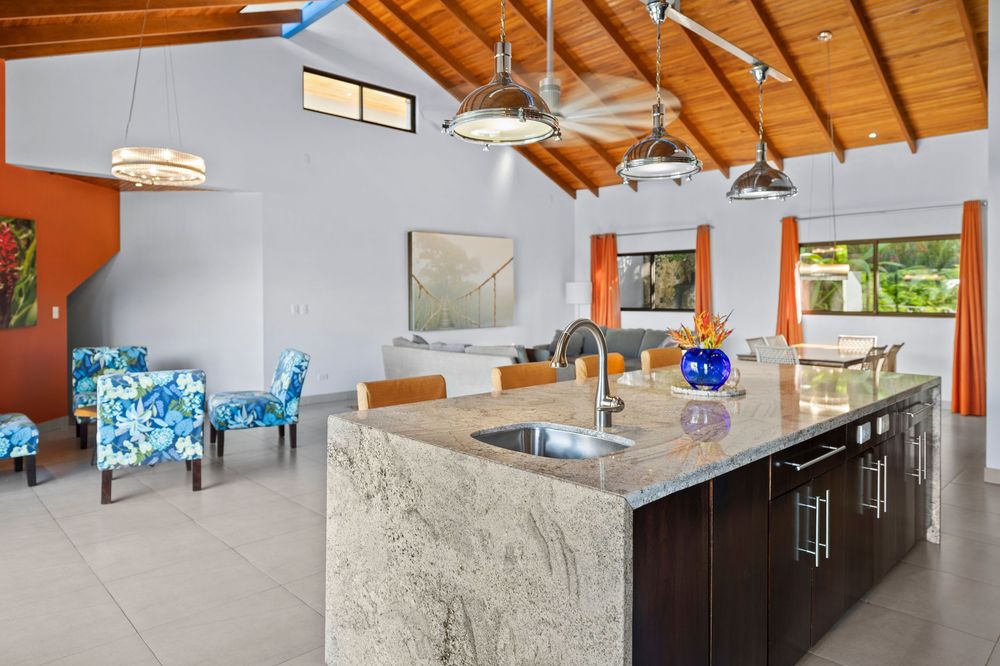 Modern kitchen island with granite countertop and sink, open to living area with vaulted wood ceiling and ceiling fans.