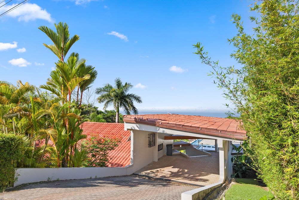 Tropical home with red tile roof, palm trees, and stunning ocean views on a sunny day.