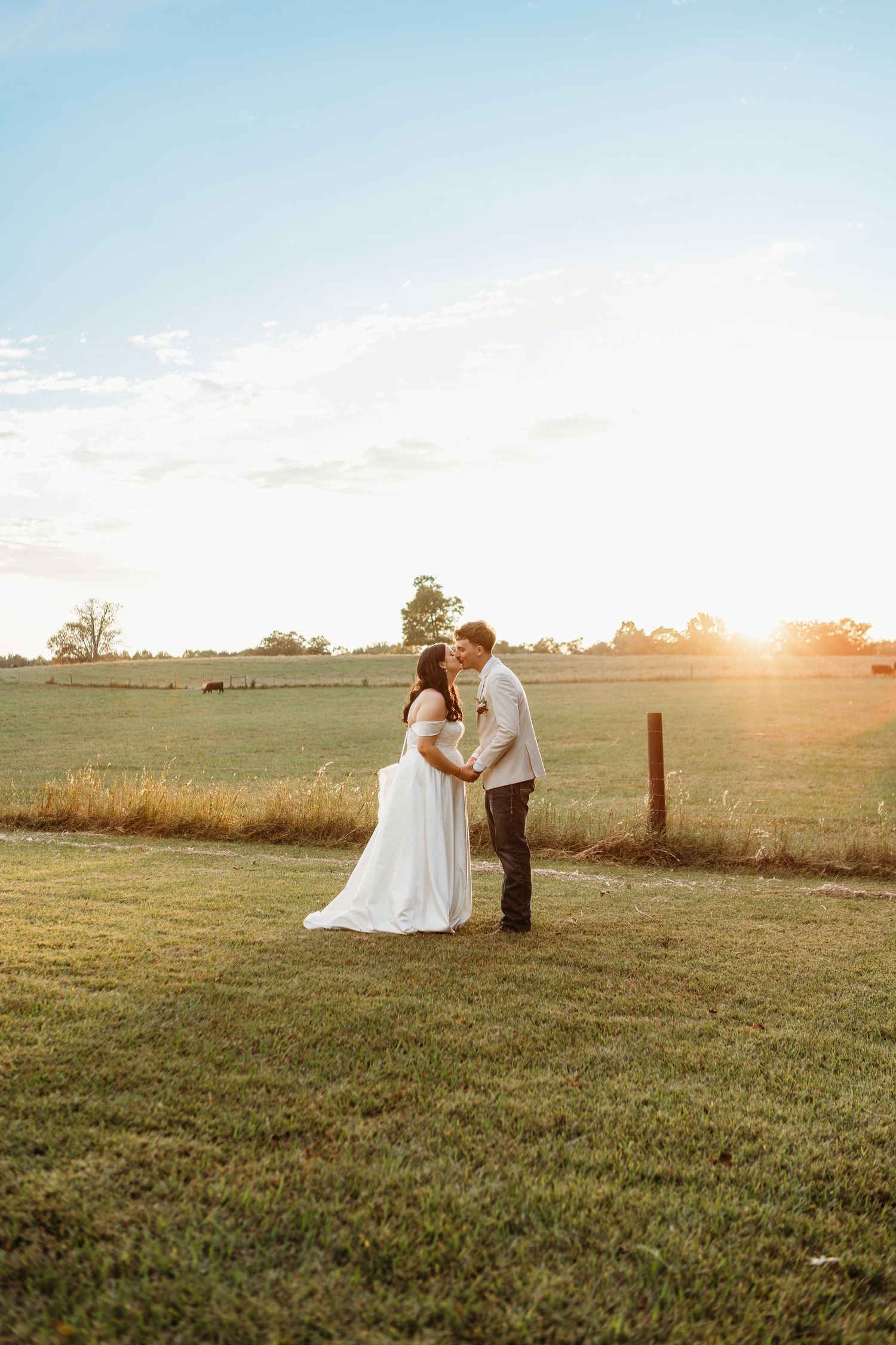 Bride and groom share a romantic moment at golden hour in a lush green farm field during their outdoor wedding.