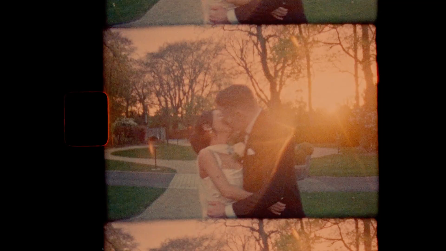 Romantic couple embracing at golden sunset in a park, captured on vintage film with warm orange tones.