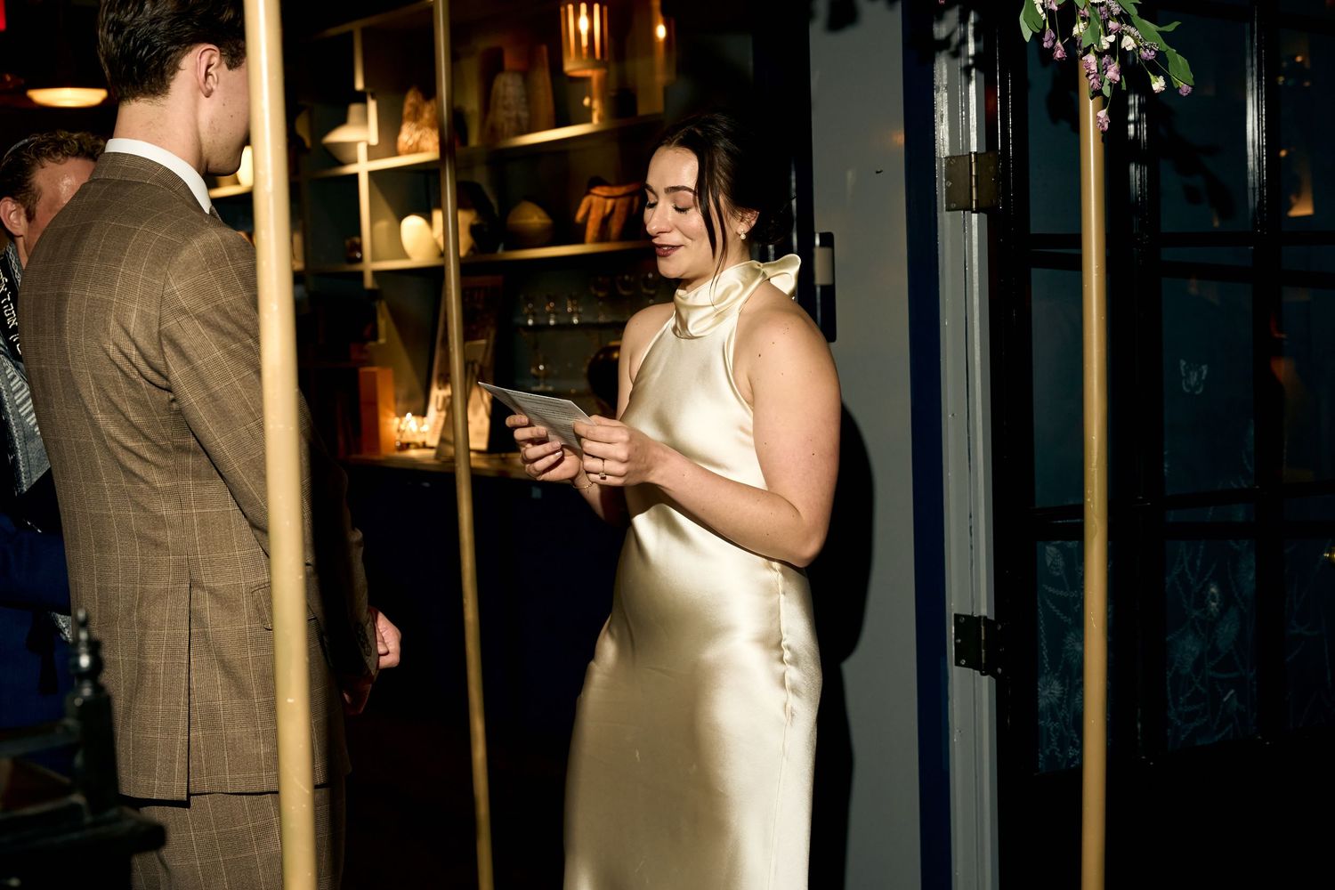 Woman in elegant ivory satin dress holding a tablet at an upscale indoor event with warm ambient lighting.