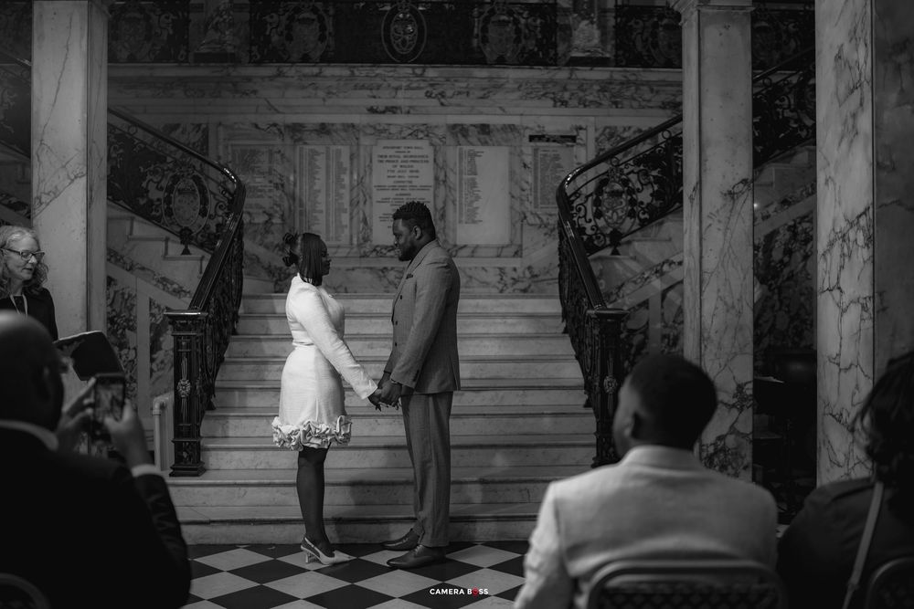 Black and white photo of a couple holding hands at the bottom of grand marble stairs during a wedding ceremony.