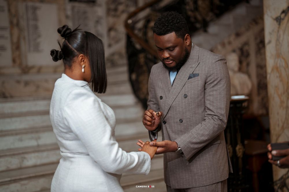 A man in a gray suit places a ring on a woman's finger during an elegant indoor proposal ceremony.