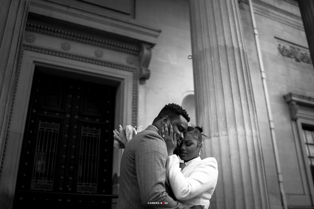Black and white photo of a couple embracing tenderly outside a grand classical building with ornate columns and doors.