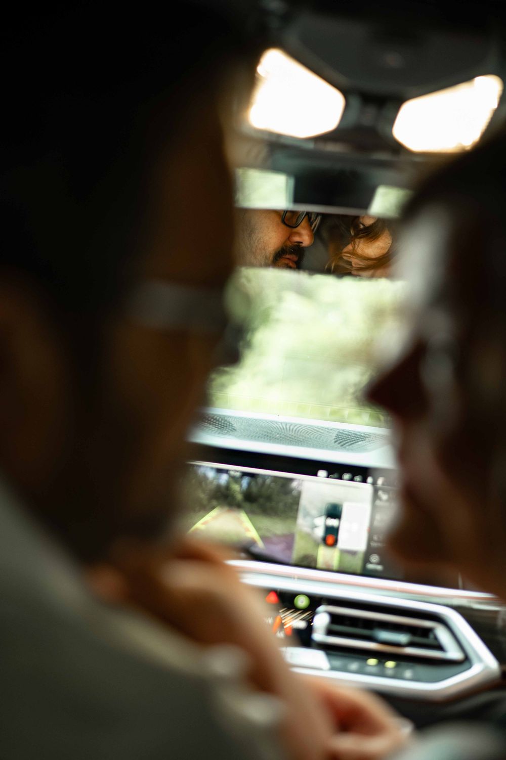 Couple nearly kissing reflected in rearview mirror inside a luxury BMW SUV interior.