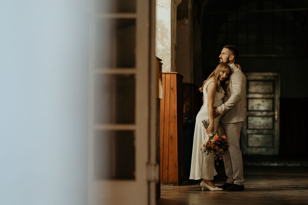 Bride and groom embracing in a doorway with warm light in a rustic venue.