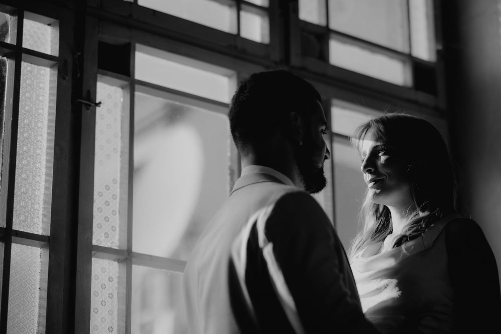 Black and white photo of bride and groom sharing an intimate moment by windows.