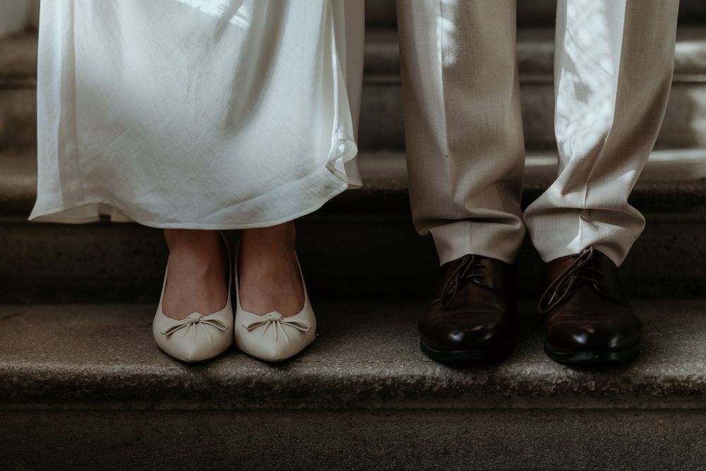 Close-up of bride in white ballet flats and groom in brown oxford shoes on stone steps.