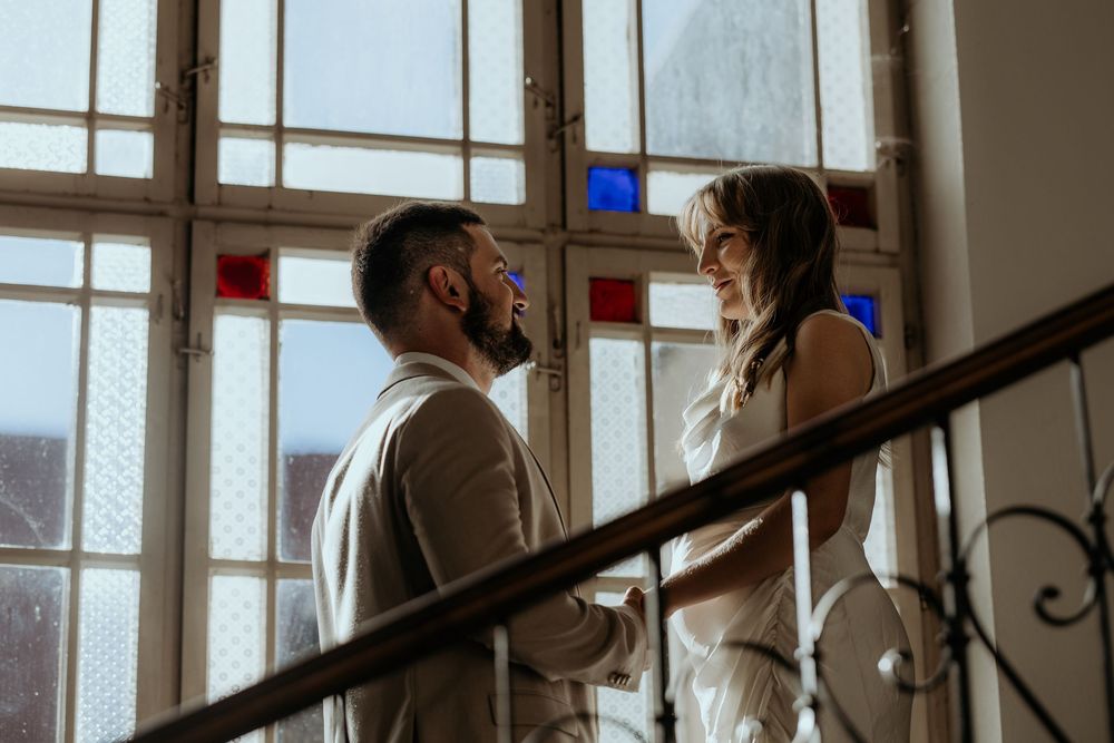 Bride and groom sharing intimate moment on staircase with colorful stained glass windows.