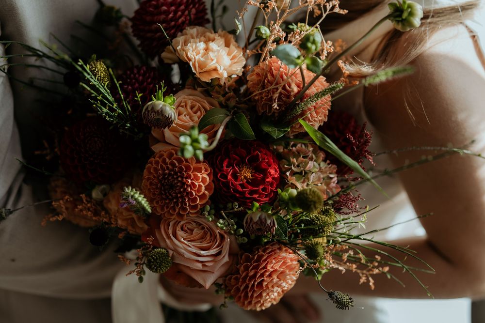 Stunning autumn wedding bouquet with burgundy dahlias, peach roses, and lush greenery.