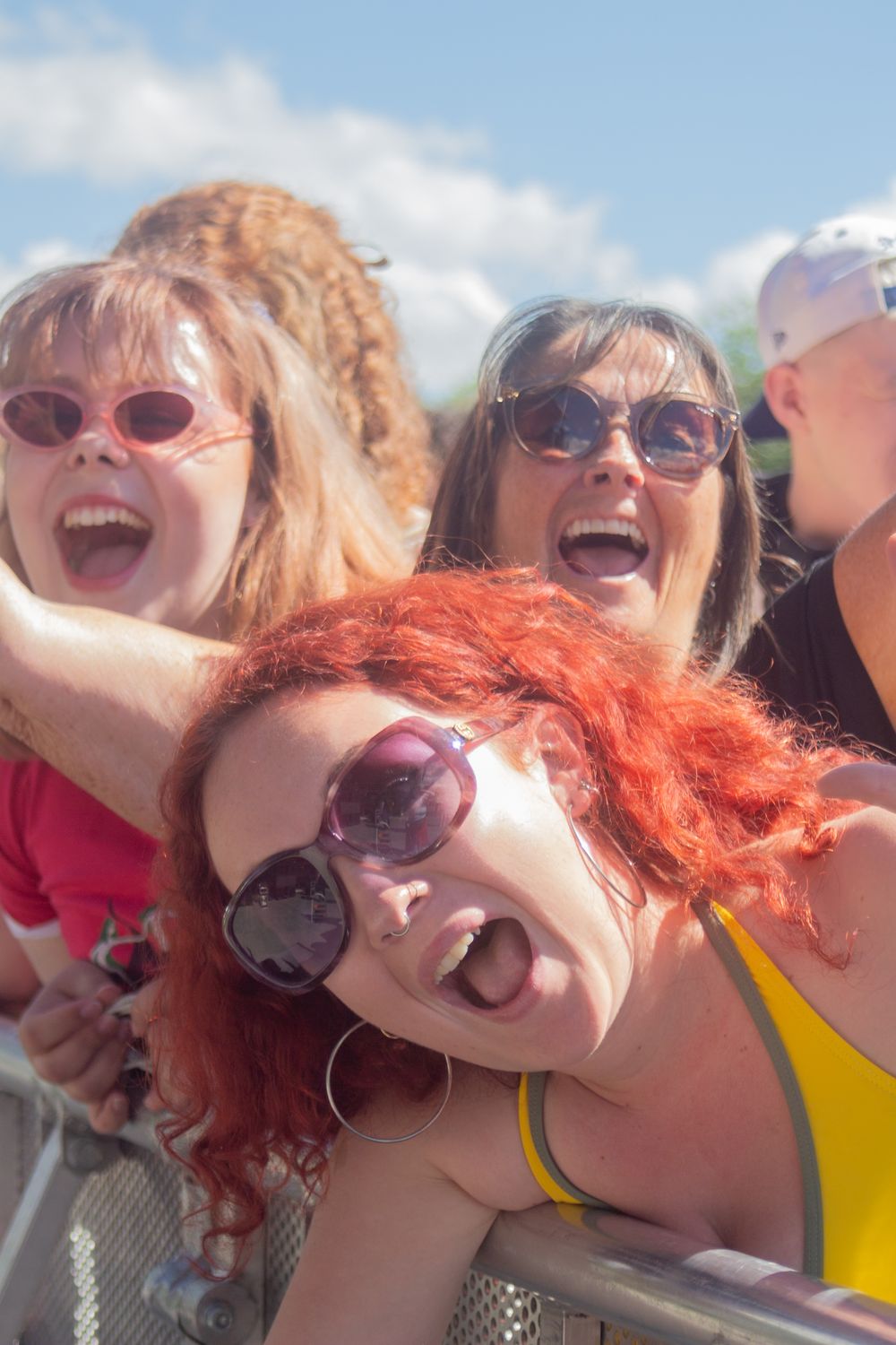 Women with sunglasses cheering and sticking out tongues at an outdoor music festival on a sunny day.