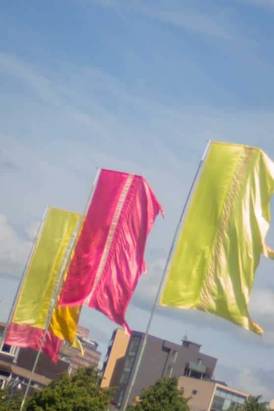 Colorful pink and yellow flags waving in the breeze at an outdoor festival on a sunny day.