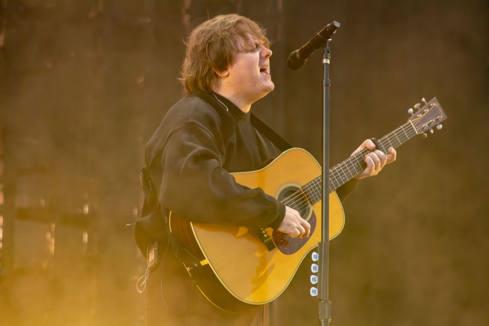 Male artist performs with yellow acoustic guitar on stage bathed in warm golden light.